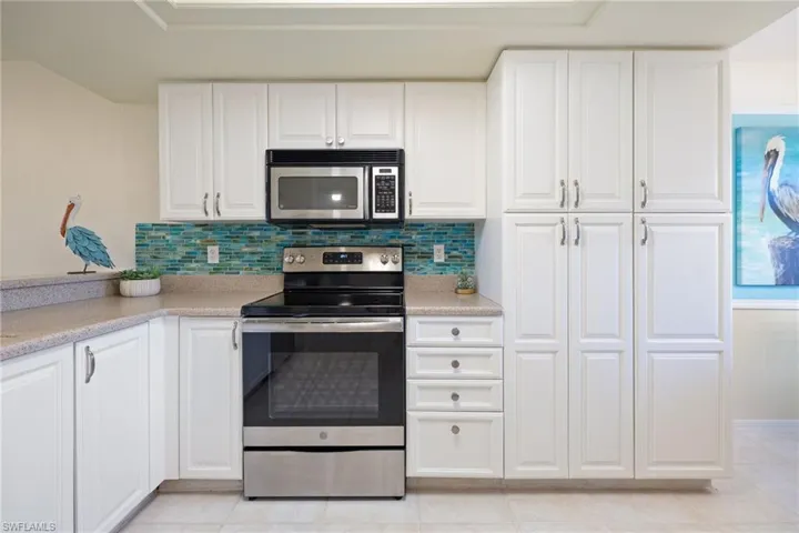 Kitchen with stainless steel appliances, white cabinetry, decorative backsplash, and light tile patterned floors.