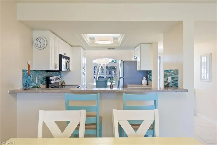 Kitchen with backsplash, a tray ceiling, white cabinets, stainless steel appliances, and a breakfast bar