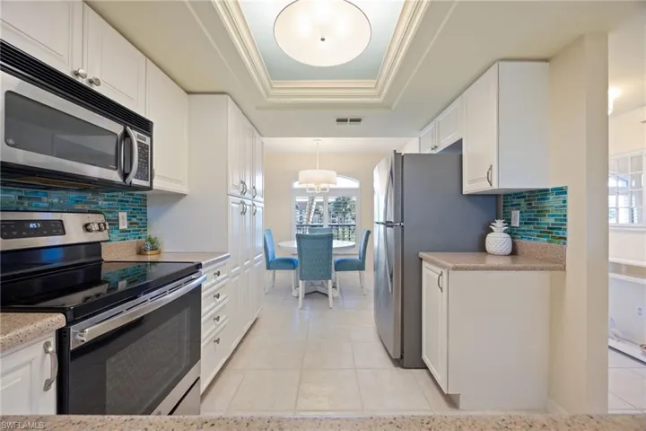 Kitchen with backsplash, a raised tray ceiling, stainless steel appliances, white cabinetry, and new light fixtures.