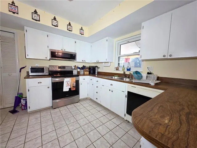 Kitchen featuring dark countertops, stainless steel appliances, white cabinetry, and light tile patterned floors