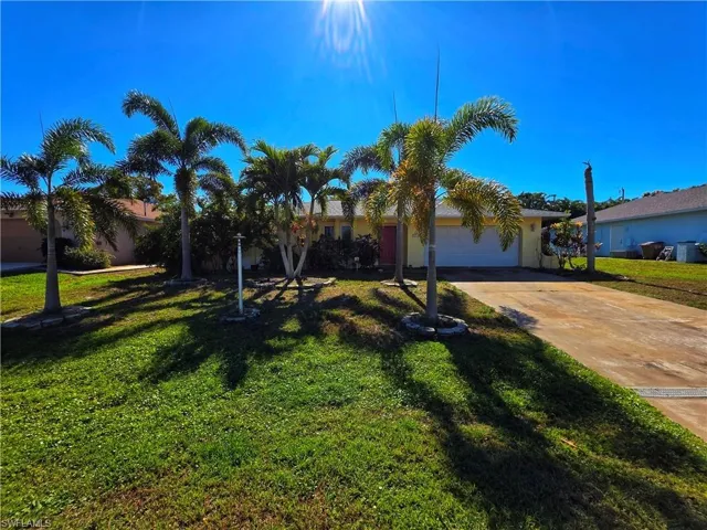 View of property hidden behind natural elements with concrete driveway, a garage, a front yard, and stucco siding