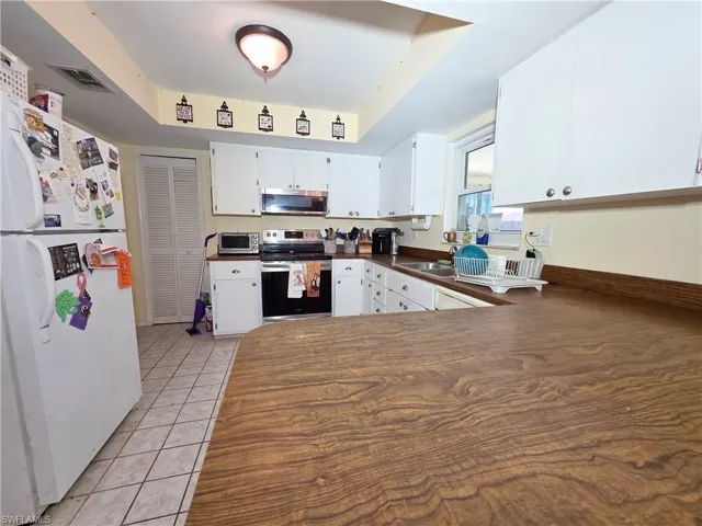 Kitchen featuring stainless steel appliances, white cabinets, light tile patterned floors, dark countertops, and a tray ceiling