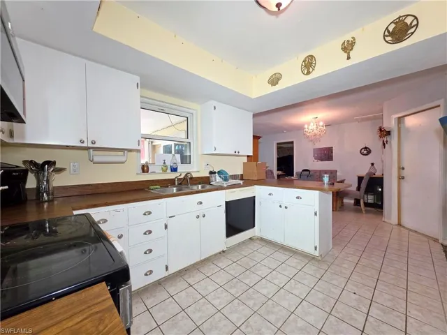 Kitchen with black / electric stove, a peninsula, white cabinetry, and a chandelier