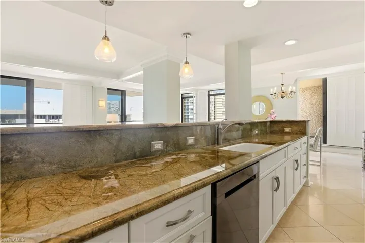 Kitchen featuring decorative backsplash, dishwasher, white cabinets, dark stone counters, and hanging lights