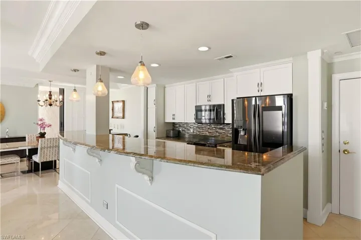 Kitchen featuring crown molding, stainless steel appliances, white cabinets, decorative backsplash, and decorative light fixtures