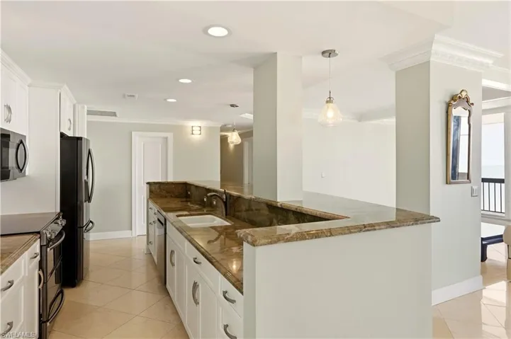 Kitchen with white cabinetry, black appliances, ornamental molding, light tile patterned flooring, and dark stone counters