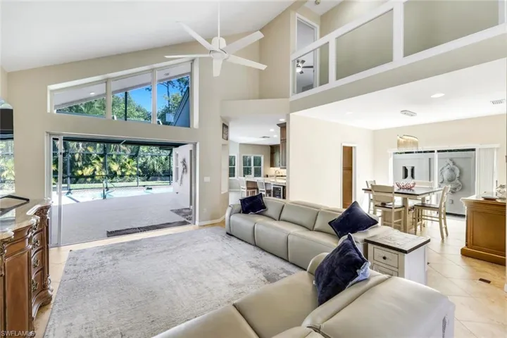 Expansive open-concept living area with soaring vaulted ceilings, abundant natural light, and seamless indoor-outdoor flow to the screened lanai and pool.