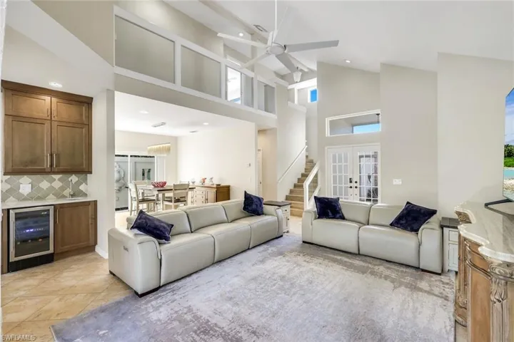 Light-filled open-concept living area featuring soaring vaulted ceilings, wet bar with wine cooler, and seamless flow to adjacent living and dining spaces.