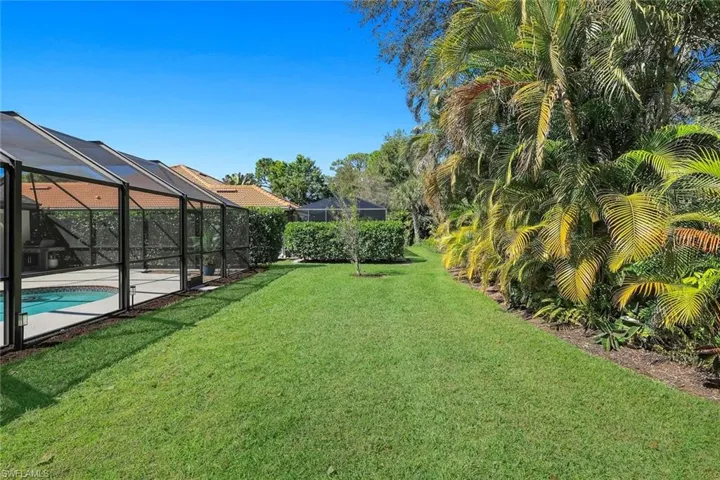Private backyard with lush landscaping and expansive green space alongside the screened pool enclosure.