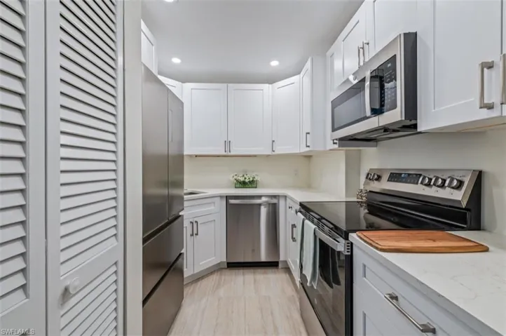 Kitchen featuring appliances with stainless steel finishes, recessed lighting, light stone countertops, white cabinetry, and tile wood floors