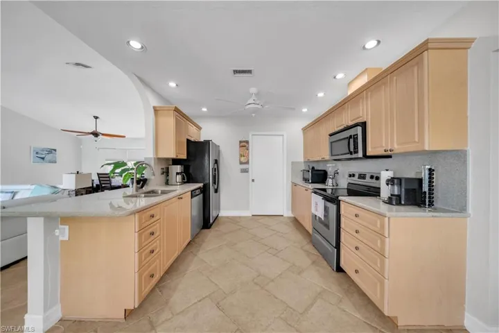 Kitchen with light brown cabinets, light stone counters, stainless steel appliances, backsplash, and ceiling fan