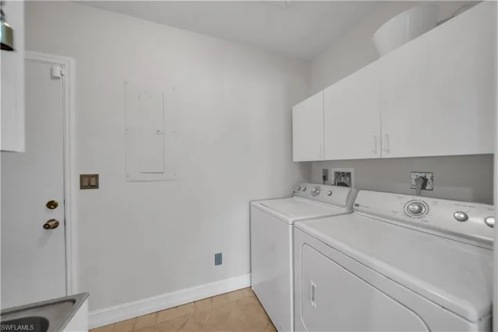 Laundry area with electric panel, cabinet space, washing machine and clothes dryer, and light tile patterned floors