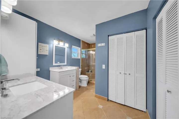 Bathroom with a closet, two vanities, a stall shower, and light tile patterned flooring
