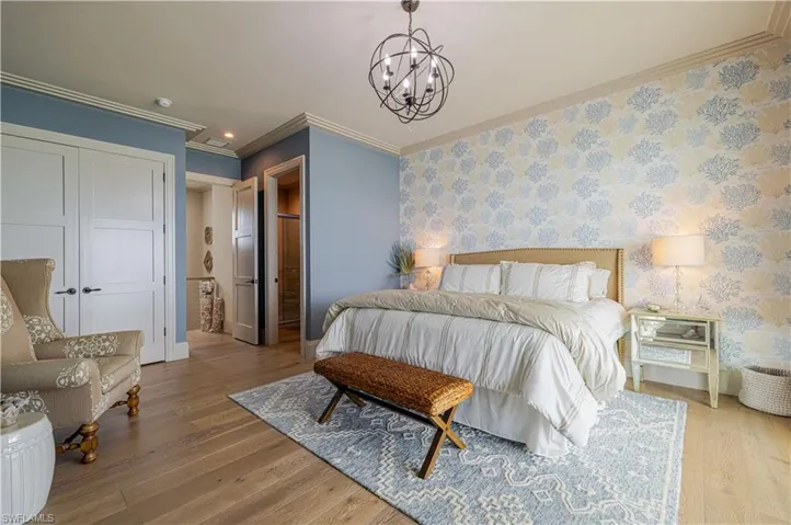 Bedroom featuring wood-finish flooring, a decorative accent wall, and crown molding