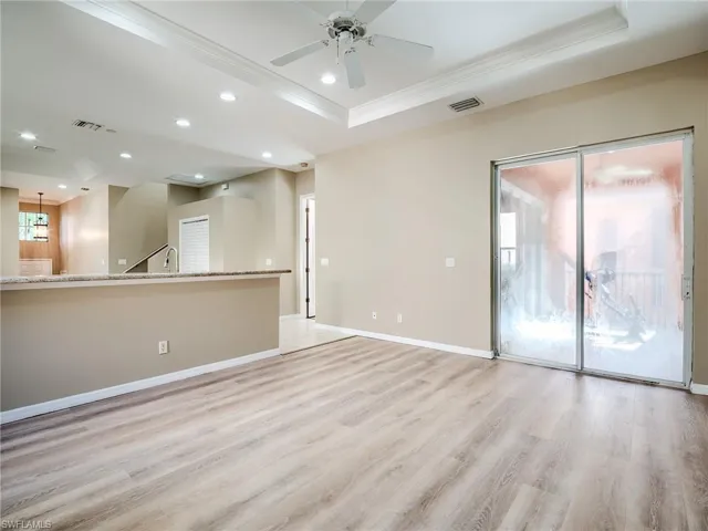 Empty room featuring light wood finished floors, recessed lighting, ceiling fan, a tray ceiling, and crown molding