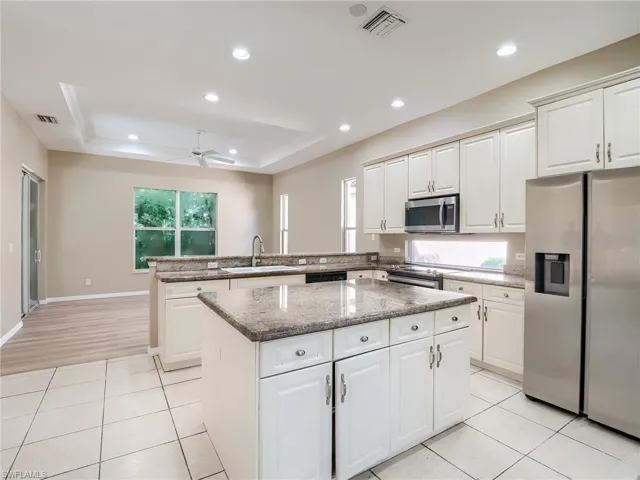 Kitchen featuring white cabinets, appliances with stainless steel finishes, light stone countertops, ceiling fan, and a tray ceiling