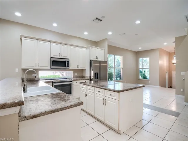 Kitchen with recessed lighting, appliances with stainless steel finishes, white cabinets, a kitchen island, and light tile patterned flooring