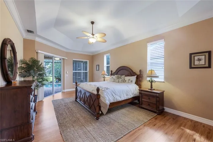 Spacious primary bedroom has beautiful wood flooring, tray ceiling and access to the pool/lanai area