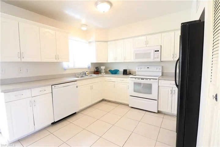 Kitchen with white appliances, sink, white cabinets, and light tile patterned floors