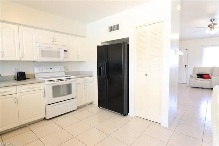 Kitchen featuring light tile patterned floors, white appliances, ceiling fan, and white cabinetry