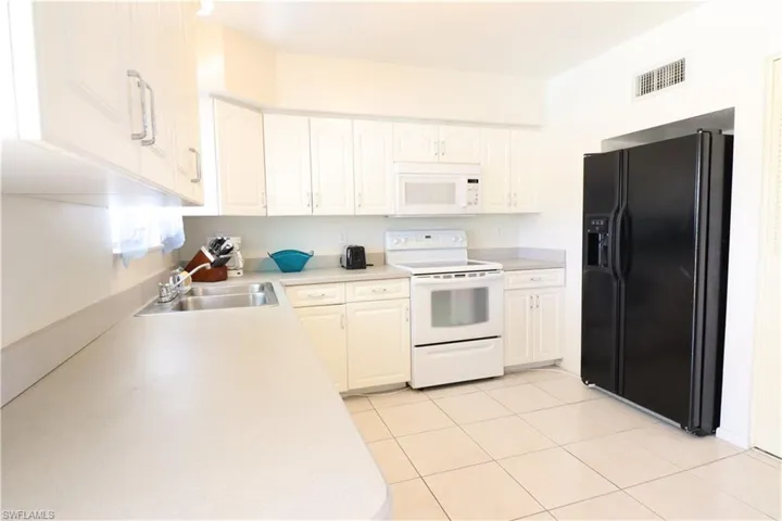 Kitchen with white appliances, sink, white cabinetry, and light tile patterned floors