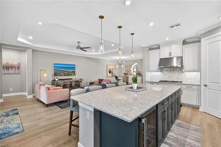 Two tone kitchen with ornamental molding, open floor plan, light stone counters, dual tone cabinets