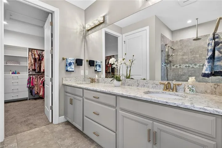Full bathroom with double vanity, a walk in closet, a tile shower, and light carpet