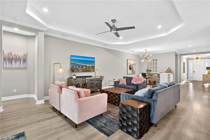 Living room featuring ceiling fan, light wood finished floors, crown molding, a tray ceiling