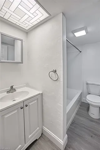 Bathroom with light wood-style flooring, vanity, shower / tub combination, and a textured wall