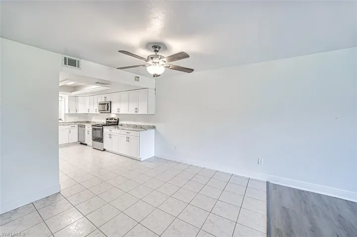 Kitchen with stainless steel appliances, white cabinets, a ceiling fan, light stone countertops, and a tray ceiling