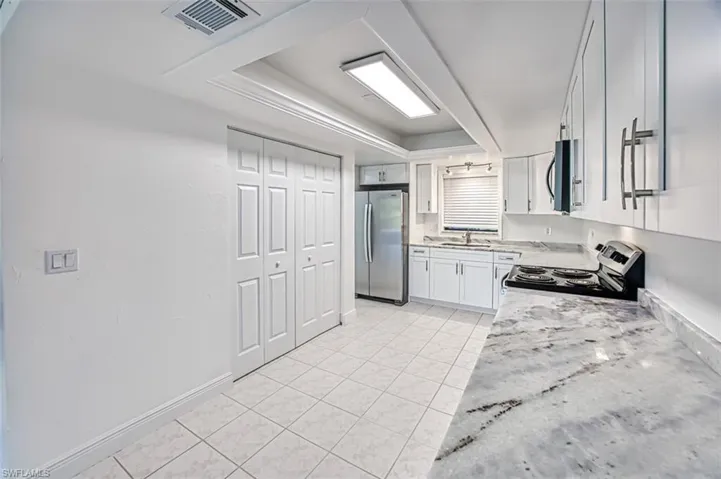 Kitchen featuring a raised ceiling, stainless steel appliances, white cabinetry, light tile patterned floors, and light stone counters