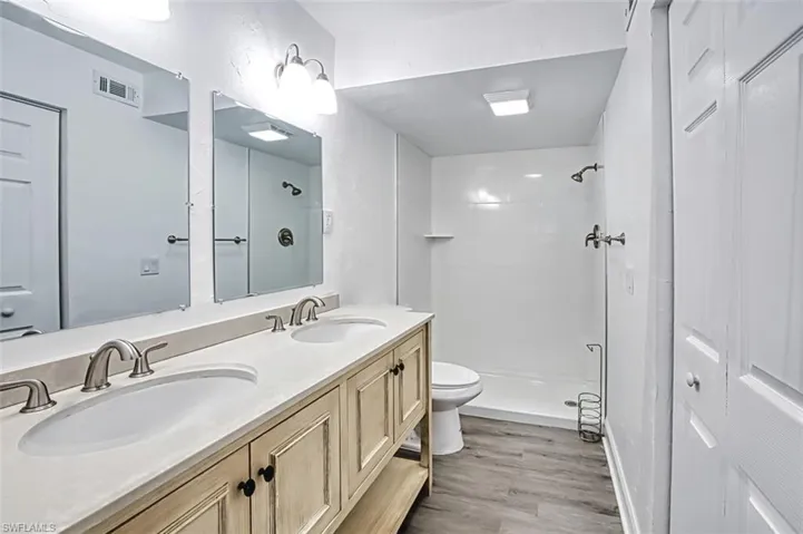 Bathroom featuring a stall shower, double vanity, and light wood-style flooring