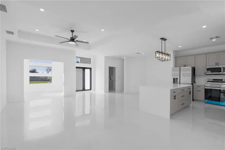 Kitchen with appliances with stainless steel finishes, decorative light fixtures, ceiling fan with notable chandelier, light tile patterned flooring, and a raised ceiling