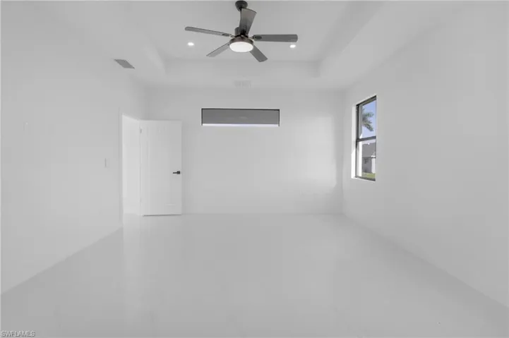 Tiled empty room with ceiling fan and a raised ceiling