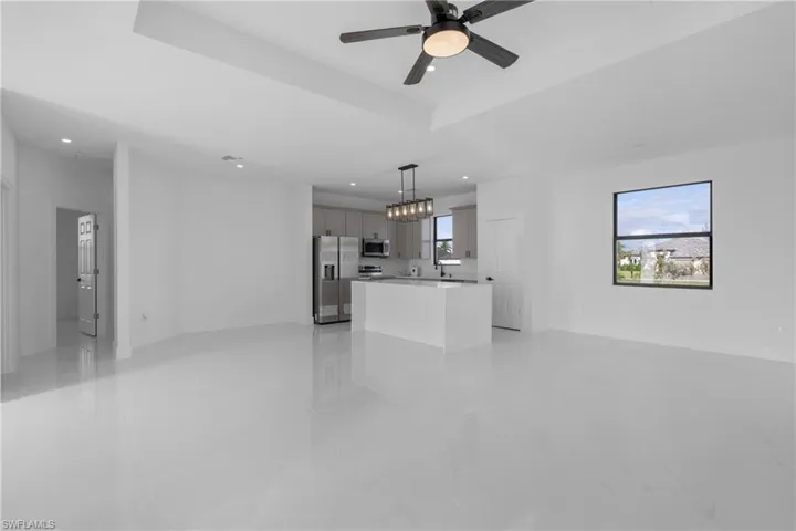 Unfurnished living room with light tile patterned flooring, ceiling fan, and a raised ceiling