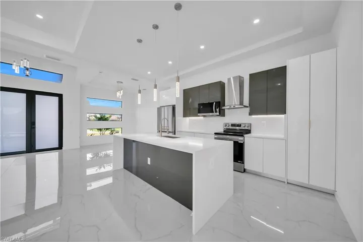Kitchen featuring stainless steel appliances, modern cabinets, light marble finish flooring, and a raised ceiling