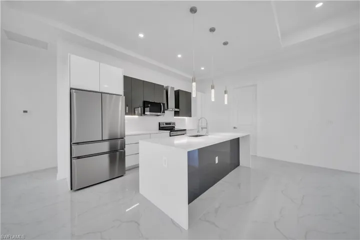 Kitchen with stainless steel appliances, a center island with sink, hanging light fixtures, light stone counters, and white cabinetry