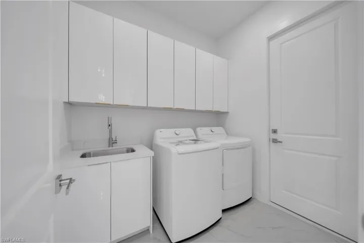 Laundry area featuring cabinet space, light marble finish floors, and washing machine and clothes dryer