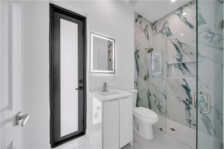 Bathroom with a marble finish shower, vanity, light marble finish flooring, and recessed lighting