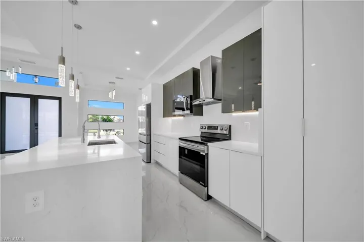 Kitchen with stainless steel appliances, modern cabinets, light marble finish floors, light stone countertops, and a center island with sink