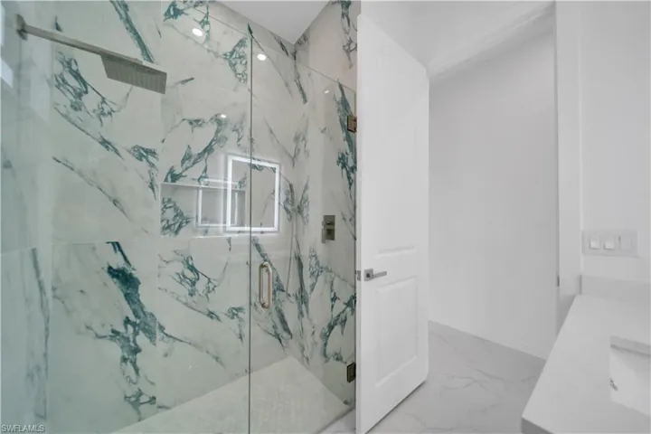 Bathroom featuring vanity, a marble finish shower, and light marble finish floors