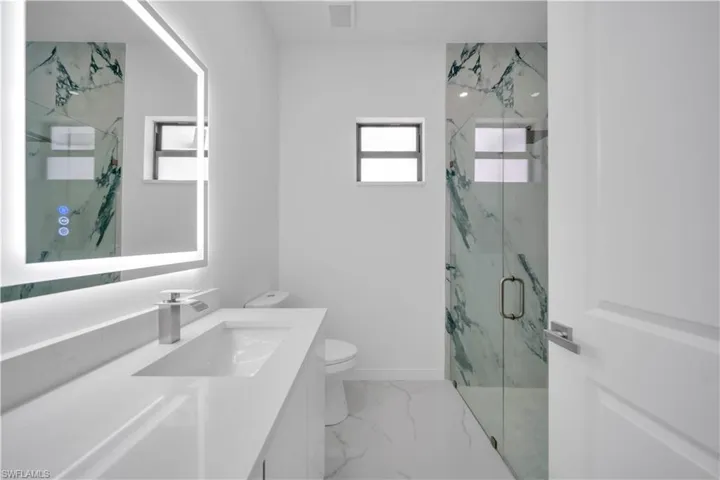 Bathroom with plenty of natural light, a marble finish shower, vanity, and light marble finish flooring