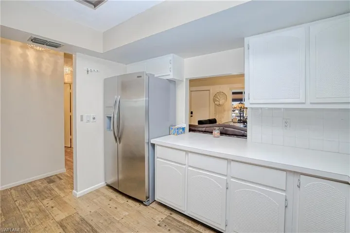 Kitchen with light countertops, stainless steel fridge, white cabinets, light wood-type flooring, and tasteful backsplash