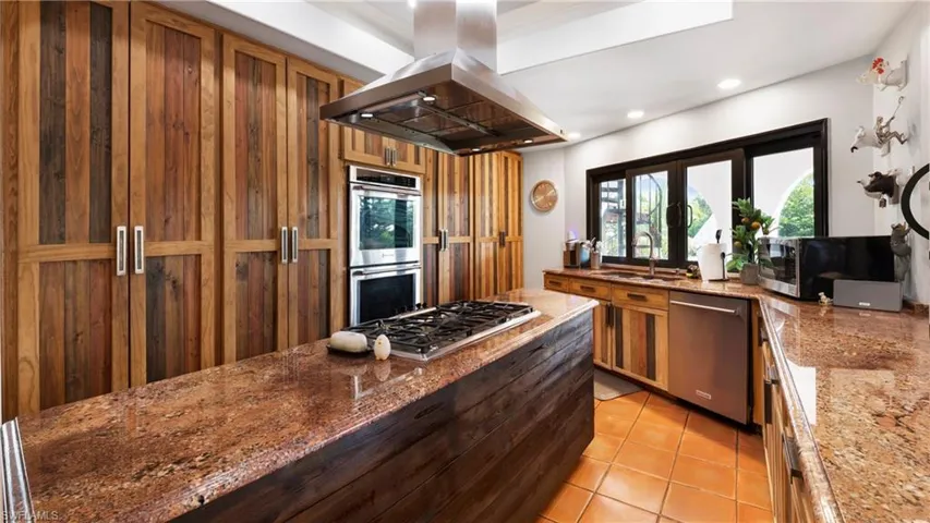 Kitchen with island range hood, dark stone counters, stainless steel appliances, light tile patterned floors, and recessed lighting