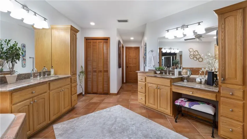 Full bathroom featuring two vanities, light tile patterned floors, a closet, tiled tub, and recessed lighting