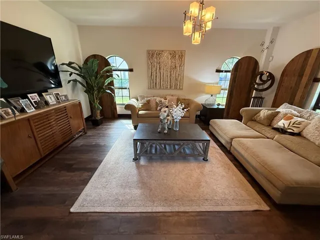 Living area featuring plenty of natural light, dark wood-style floors, arched walkways, and a chandelier