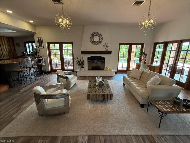 Living room with a chandelier, french doors, wood finished floors, a fireplace, and recessed lighting