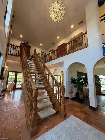 Staircase featuring a towering ceiling, a chandelier, arched walkways, recessed lighting, and tile patterned floors