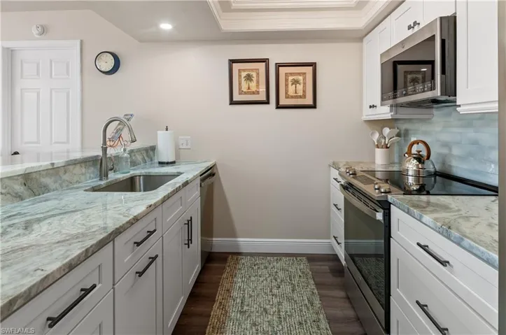 Kitchen featuring light stone counters, crown molding, stainless steel appliances, sink, and white cabinets