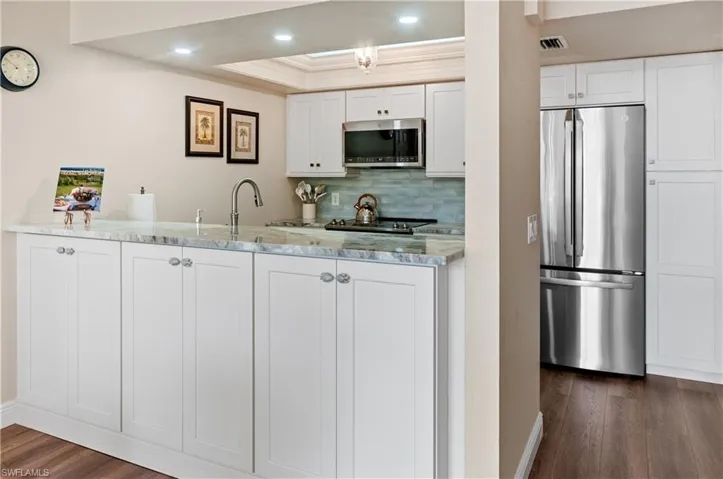 Kitchen with stainless steel appliances, white cabinets, tasteful backsplash, dark hardwood / wood-style floors, and light stone countertops